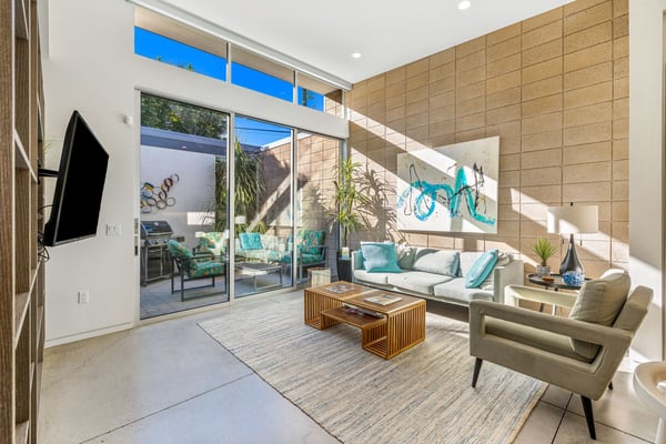 Modern living room with cork accent wall, cream sofa with turquoise pillows, sliding glass doors opening to patio with grill and seating