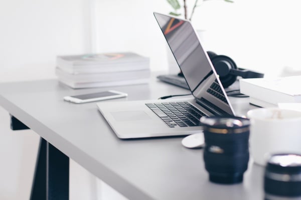 Modern workspace with laptop, tablet, smartphone, headphones, coffee cup, and potted plant on white desk