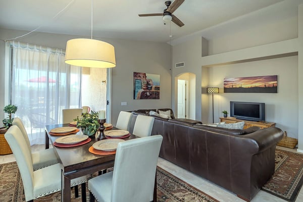 Open-plan living and dining area with brown leather sofa, dark wood dining table, cream chairs, pendant light, and flat-screen TV.