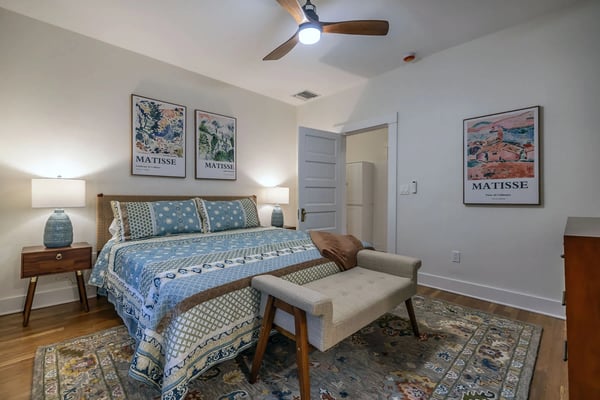 Styled bedroom with woven headboard, layered rugs, and Matisse prints in a premium Tucson vacation rental