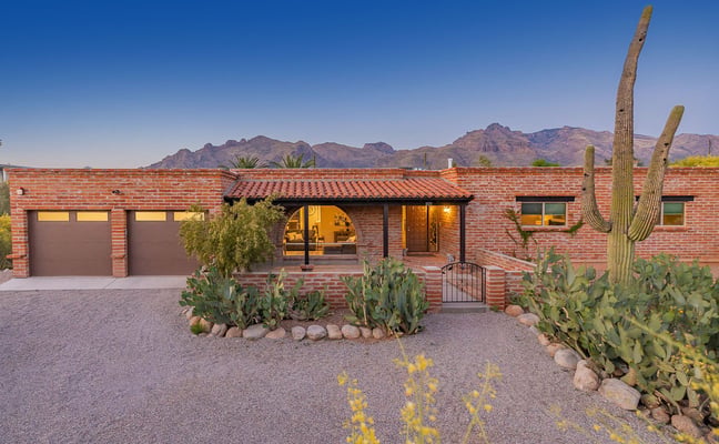 Red brick desert home with arched entry, double garage, and saguaro cacti in front yard with mountain backdrop